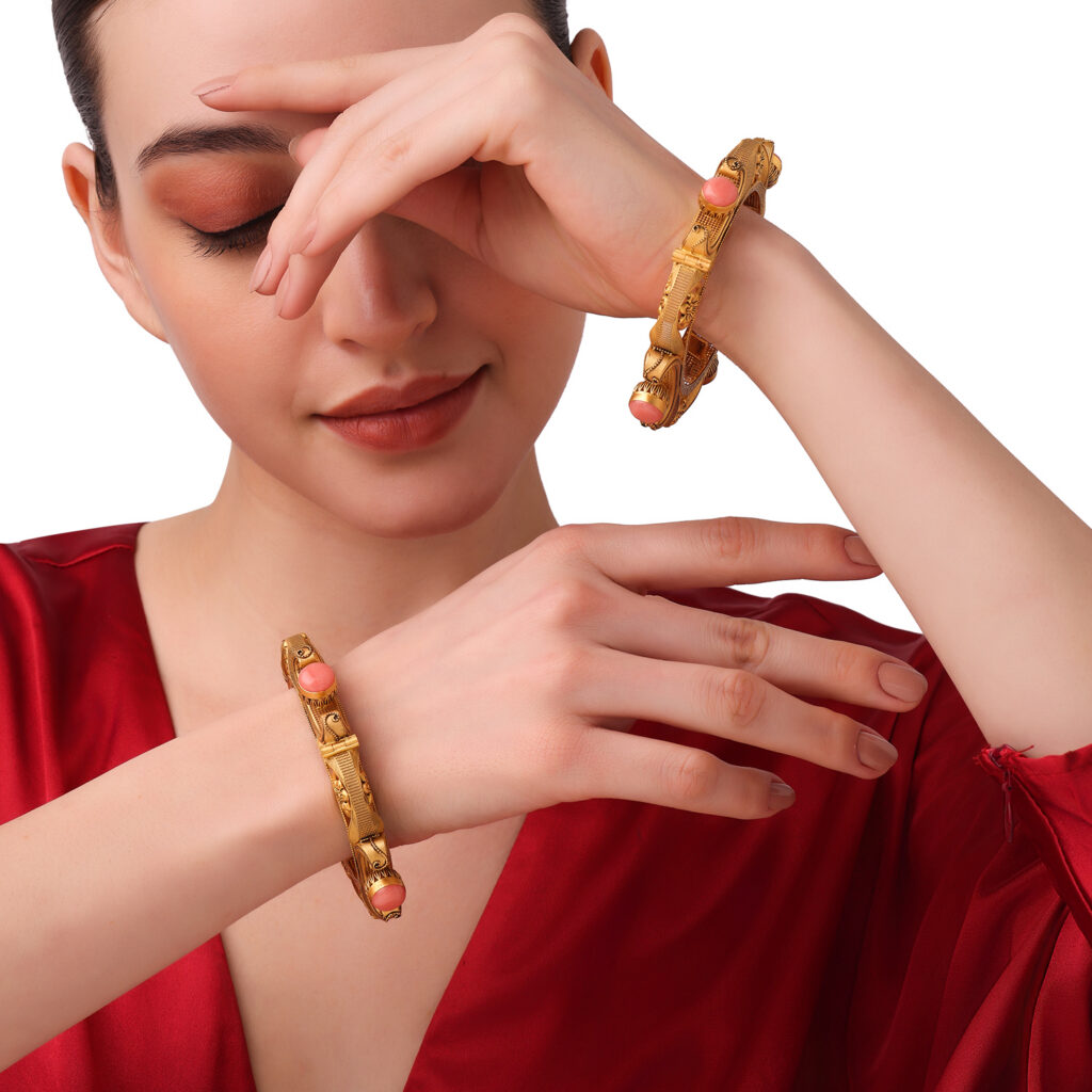 Traditional gold bangles featuring intricate filigree detailing with coral gemstone accents, elegantly styled on a woman’s wrists.